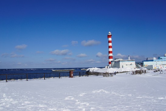 雪の積もった海岸に立つ赤と白の灯台