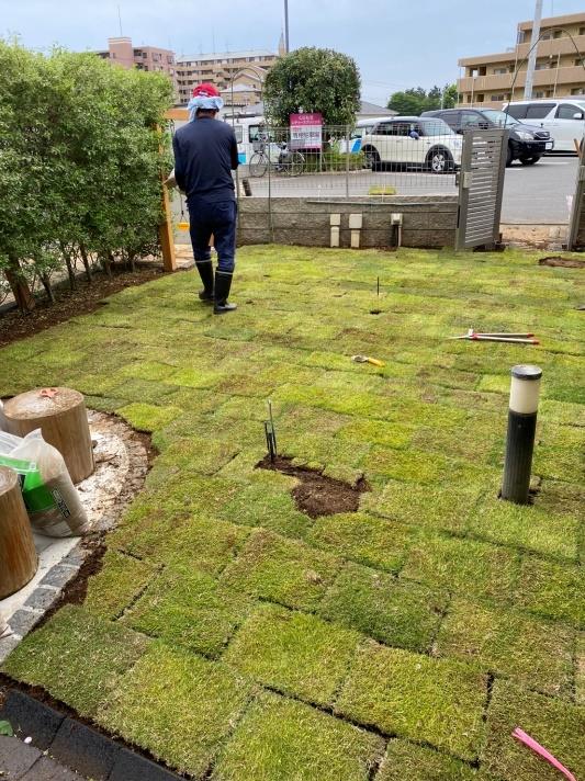 芝生を敷き詰めた庭を歩く作業員の写真