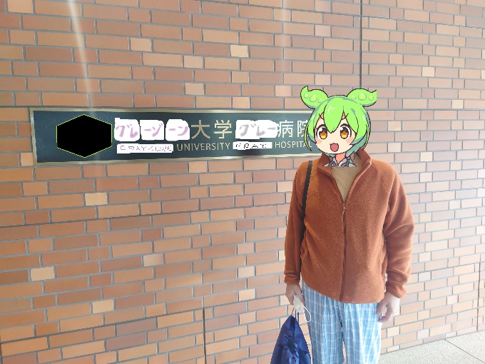 大学病院の入口看板の前に立つ人物の写真（顔はキャラクターイラストで隠されている）